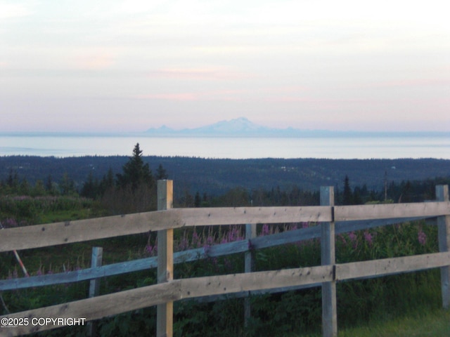 yard at dusk featuring a water and mountain view, fence, and a wooded view