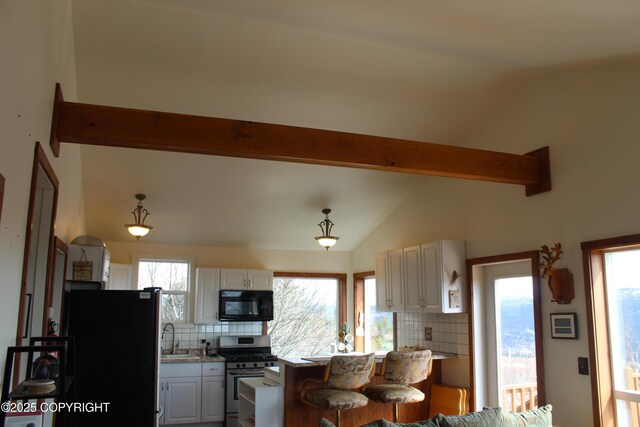 kitchen featuring freestanding refrigerator, black microwave, stainless steel gas range, vaulted ceiling with beams, and a sink