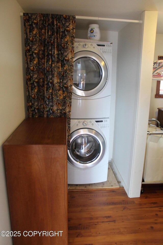 clothes washing area with stacked washer / drying machine, wood finished floors, and laundry area