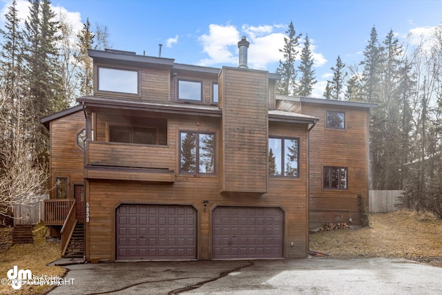 rear view of property with an attached garage, a chimney, and aphalt driveway