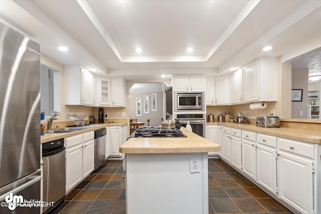 kitchen with appliances with stainless steel finishes, white cabinets, a raised ceiling, and stone tile floors