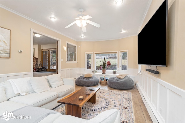 living room featuring crown molding, a ceiling fan, wainscoting, and a decorative wall