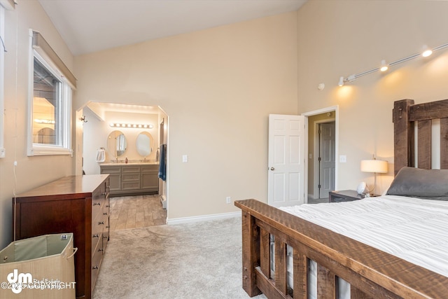 bedroom with high vaulted ceiling, light colored carpet, baseboards, and ensuite bath