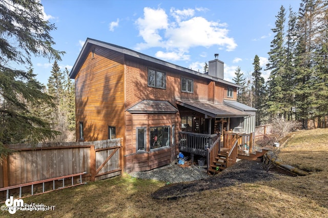rear view of house with fence, a wooden deck, a chimney, and a lawn