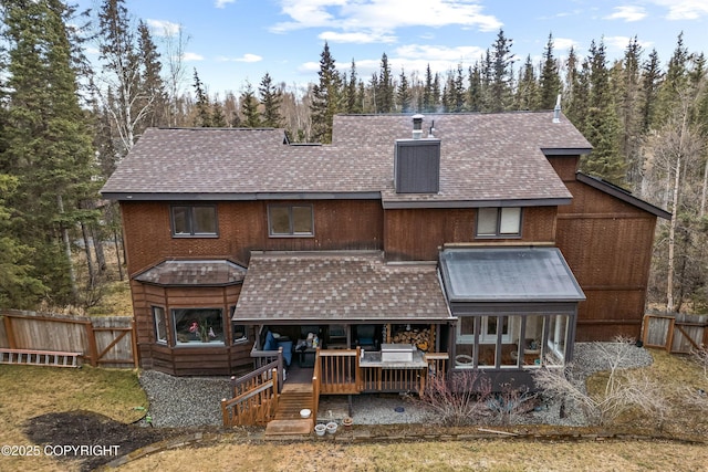 back of property with fence, a shingled roof, and a deck