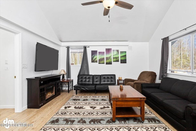 living area with ceiling fan, baseboards, vaulted ceiling, light wood-type flooring, and a lit fireplace