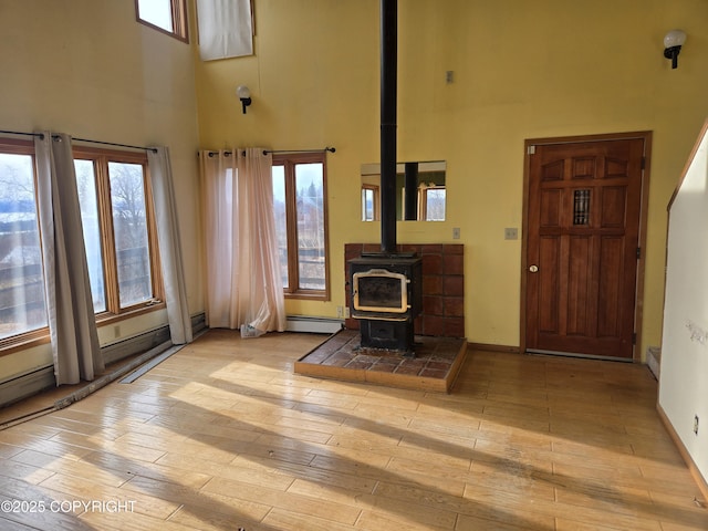 unfurnished living room featuring a high ceiling, a baseboard radiator, a wood stove, and hardwood / wood-style floors