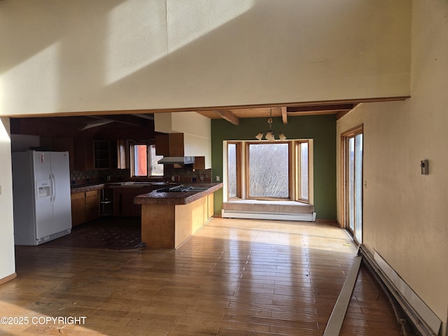kitchen with a peninsula, dark countertops, beamed ceiling, white refrigerator with ice dispenser, and a baseboard radiator