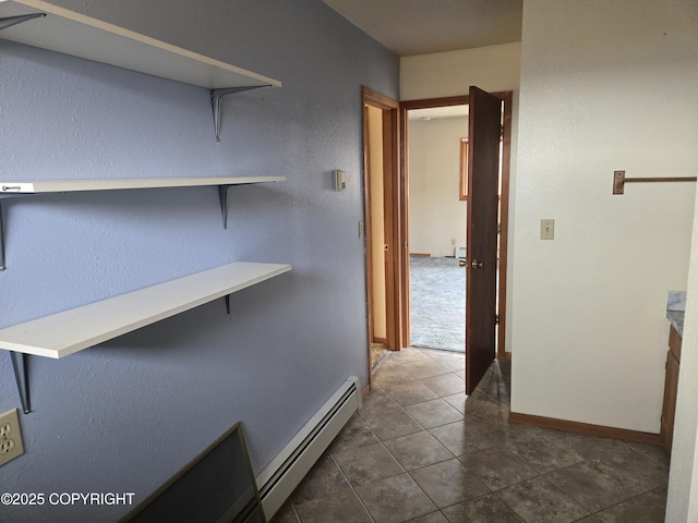 corridor featuring dark tile patterned floors, baseboards, and a baseboard heating unit