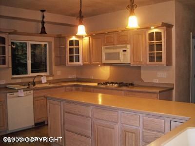 kitchen with hanging light fixtures, a sink, white appliances, light countertops, and glass insert cabinets