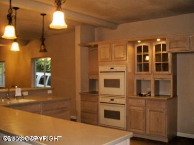kitchen with hanging light fixtures, beam ceiling, a sink, double oven, and light countertops