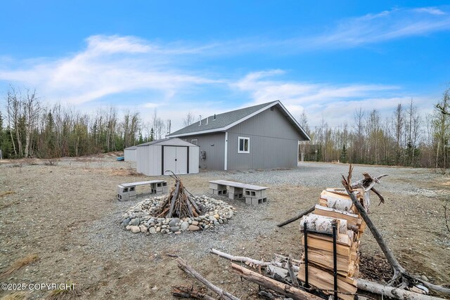 back of property featuring an outdoor structure, a fire pit, and a shed