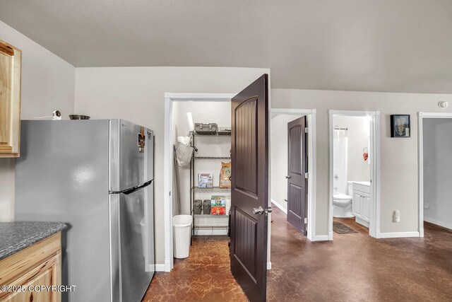 kitchen with baseboards, freestanding refrigerator, concrete floors, and dark countertops