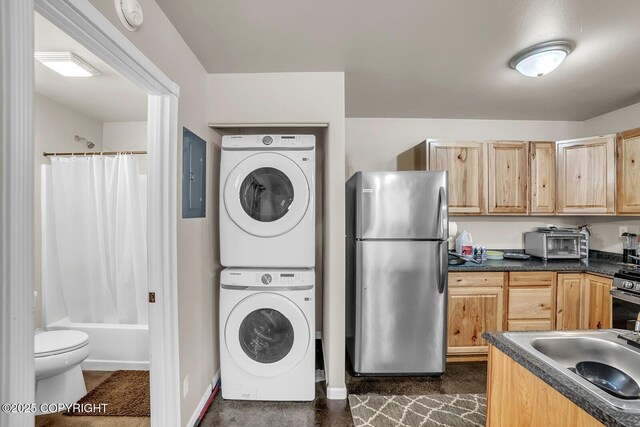 interior space with freestanding refrigerator, light brown cabinetry, stacked washing maching and dryer, and dark countertops