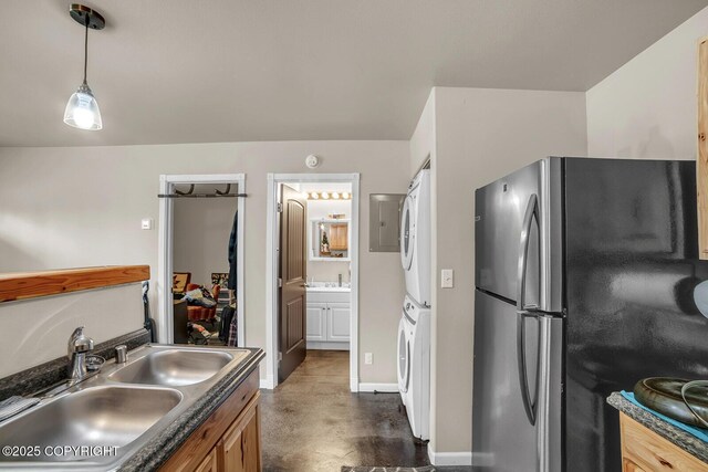 kitchen featuring concrete flooring, stacked washer / drying machine, dark countertops, a sink, and freestanding refrigerator