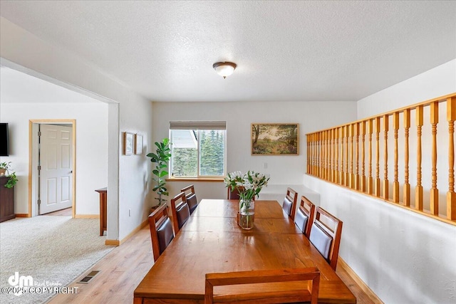 dining room featuring light wood-style flooring, visible vents, and a textured ceiling