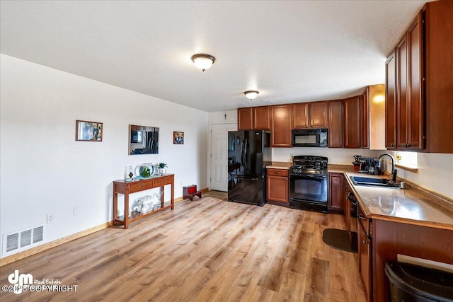 kitchen featuring a sink, brown cabinetry, light wood-type flooring, visible vents, and black appliances