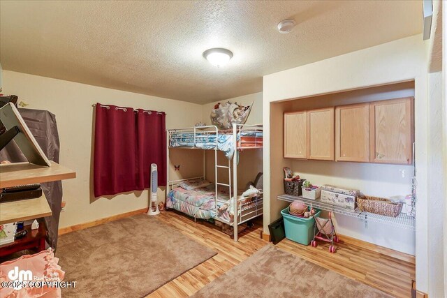 bedroom with light wood finished floors, a textured ceiling, and baseboards