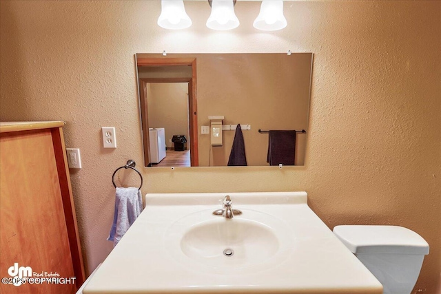 bathroom featuring toilet, vanity, and a textured wall