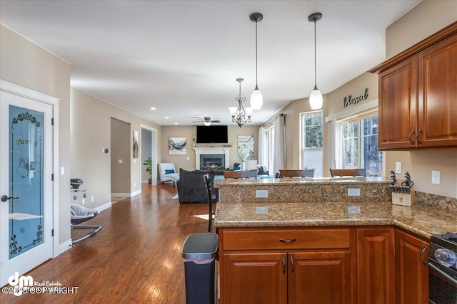 7865 S Settlers Bay Dr, Wasilla, AK 99623 - kitchen featuring brown cabinetry, hanging light fixtures, a fireplace, a peninsula, and dark wood-style floors