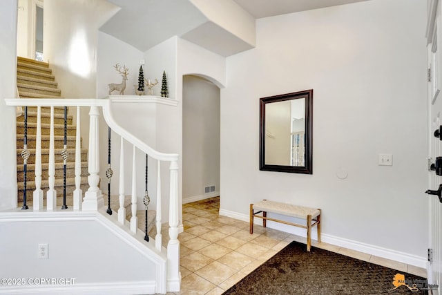 tiled entrance foyer with visible vents, arched walkways, stairs, and baseboards