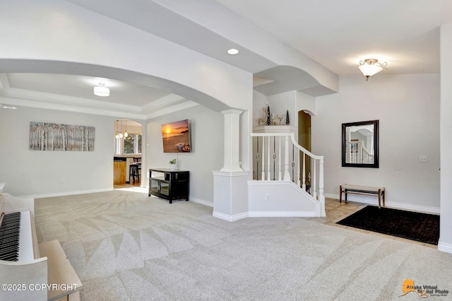 living room with light colored carpet, arched walkways, baseboards, a raised ceiling, and stairs