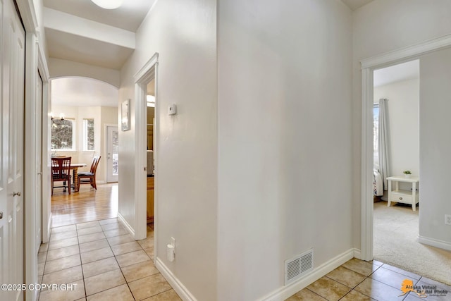 hallway with arched walkways, baseboards, visible vents, and light tile patterned floors