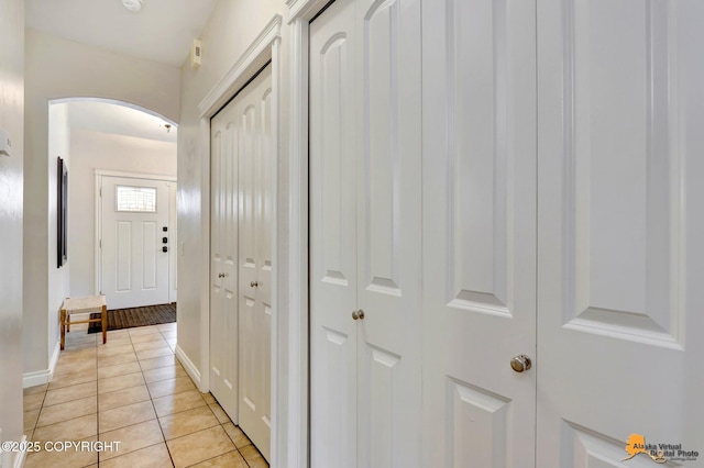 hallway with arched walkways, baseboards, and light tile patterned floors