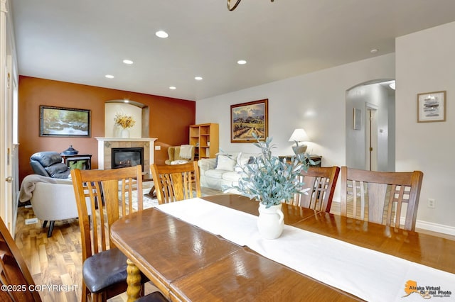 dining room featuring arched walkways, a glass covered fireplace, recessed lighting, baseboards, and wood finished floors