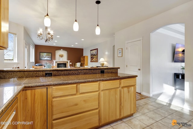 kitchen featuring pendant lighting, a glass covered fireplace, light tile patterned flooring, open floor plan, and arched walkways