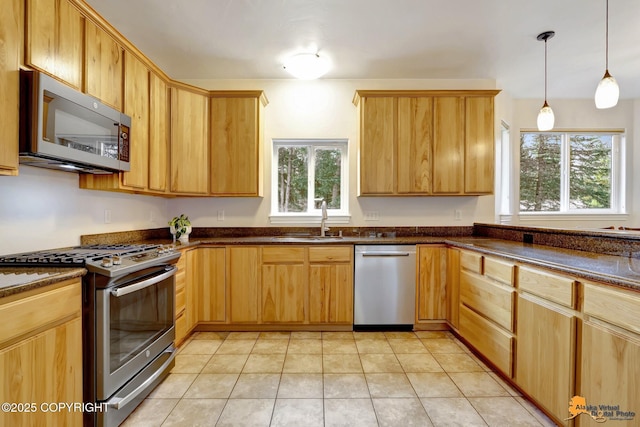 kitchen with hanging light fixtures, a sink, light tile patterned floors, dark stone counters, and stainless steel appliances