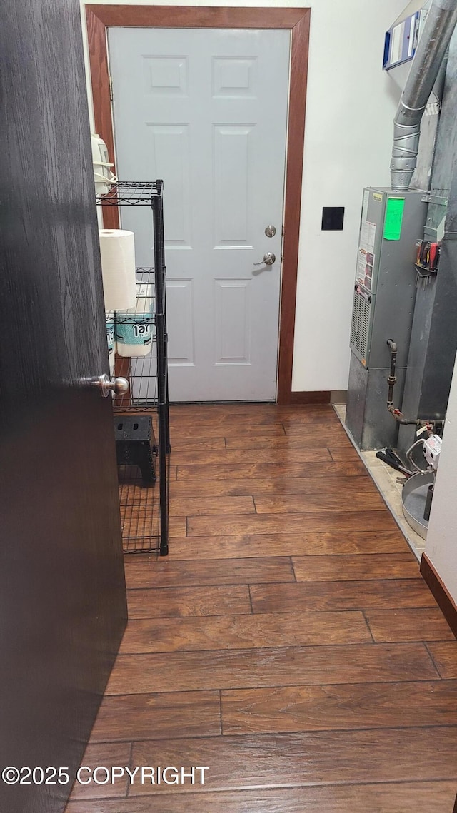 corridor featuring baseboards, heating unit, and wood finished floors