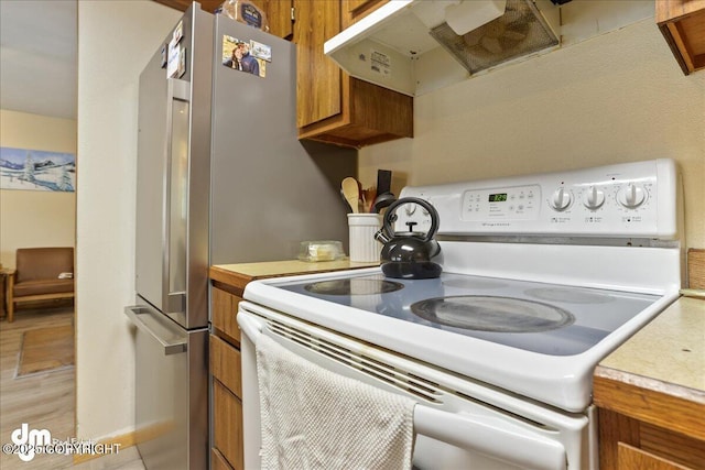 337 Alta Dr, Girdwood, AK 99587 - kitchen with freestanding refrigerator, electric range, light countertops, under cabinet range hood, and brown cabinets