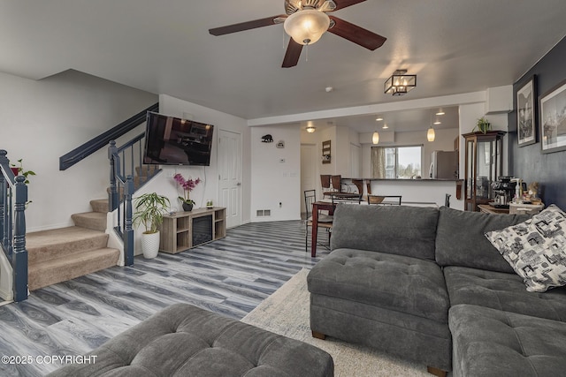 living room with a ceiling fan, stairway, visible vents, and wood finished floors