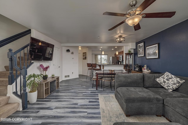 living area with stairway, wood finished floors, and ceiling fan