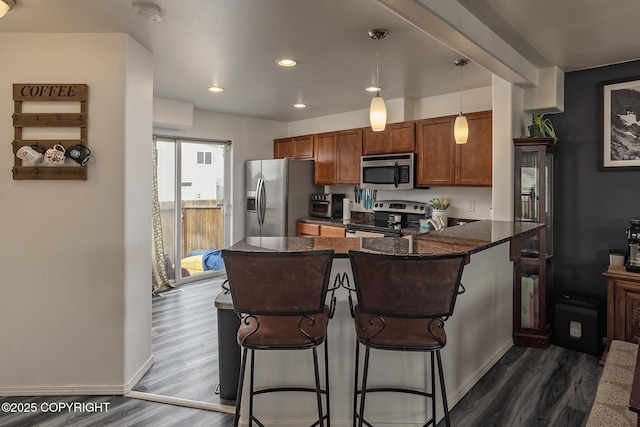 kitchen with dark wood-style flooring, stainless steel appliances, a peninsula, and brown cabinets