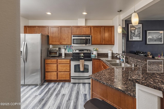 kitchen with brown cabinetry, a sink, a peninsula, light wood-style floors, and appliances with stainless steel finishes