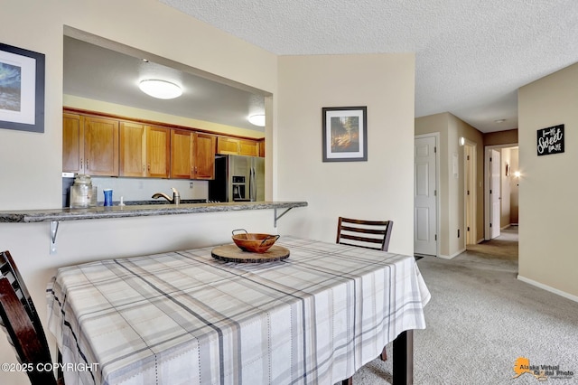dining area featuring a textured ceiling, baseboards, and light carpet