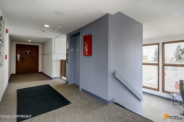 hallway featuring carpet floors, a textured ceiling, elevator, and an upstairs landing