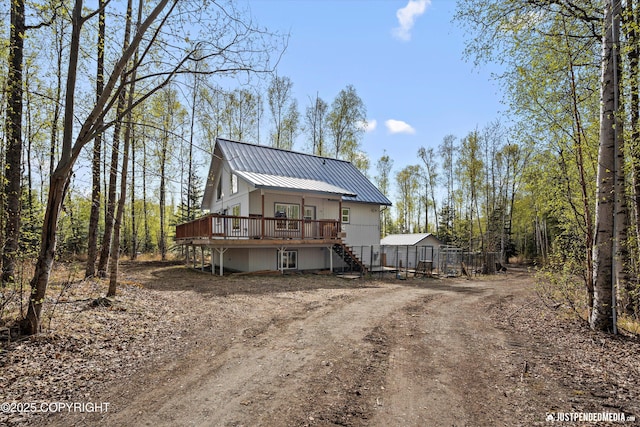 rear view of property with metal roof, a wooden deck, stairs, and driveway