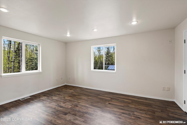 unfurnished room featuring visible vents, a healthy amount of sunlight, and dark wood-style floors