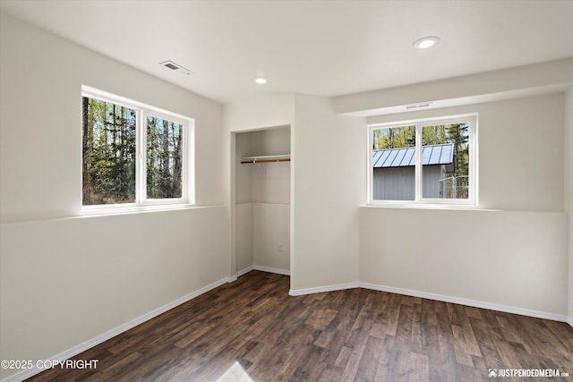 unfurnished bedroom featuring baseboards, multiple windows, visible vents, and wood finished floors