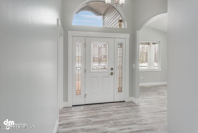 entryway featuring baseboards, arched walkways, wood finished floors, and vaulted ceiling