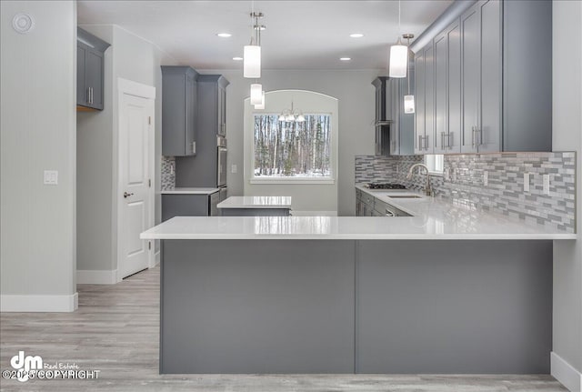 kitchen featuring a peninsula, a sink, gray cabinets, and tasteful backsplash