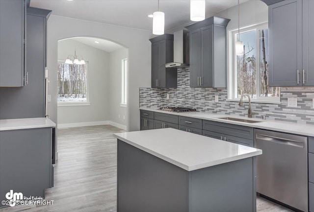 kitchen featuring baseboards, wall chimney range hood, a sink, gray cabinetry, and stainless steel appliances