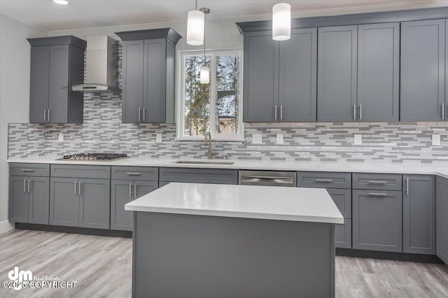 kitchen featuring wall chimney range hood, light wood-type flooring, a sink, light countertops, and stainless steel appliances