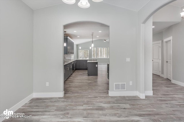 kitchen with arched walkways, a ceiling fan, baseboards, wood finished floors, and visible vents