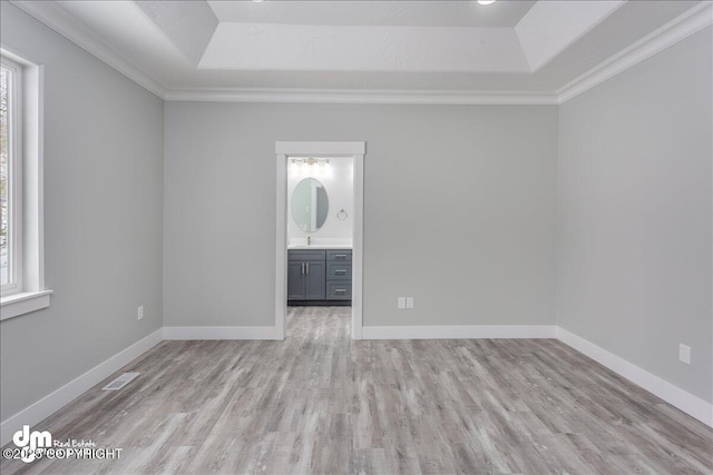 empty room featuring a raised ceiling, baseboards, light wood-style flooring, and visible vents