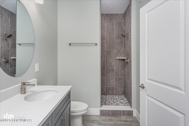full bathroom featuring wood finished floors, vanity, baseboards, toilet, and tiled shower