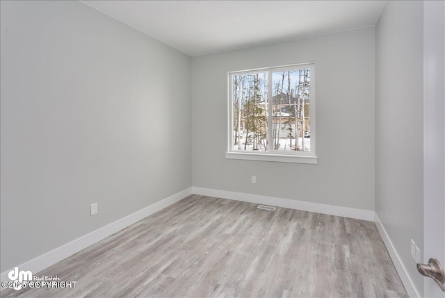 spare room with baseboards, visible vents, and wood finished floors